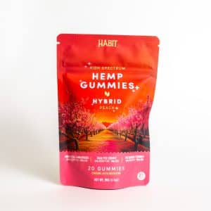 A red resealable bag labeled “Habit - High Spectrum HYB Peach,” containing 20 gummies, features illustrated peach blossoms and product details on the front.