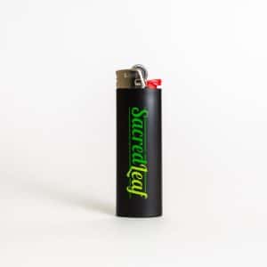 The Sacred Leaf Branded Lighter is black with a metal top and red ignition button, featuring "Sacredleaf" in green lettering on the front.