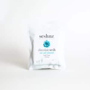 A white package labeled "SESHNZ SEA SALT ALMOND Mushroom Chocolate - Half Bar" featuring a blue rose design stands upright against a plain white background.